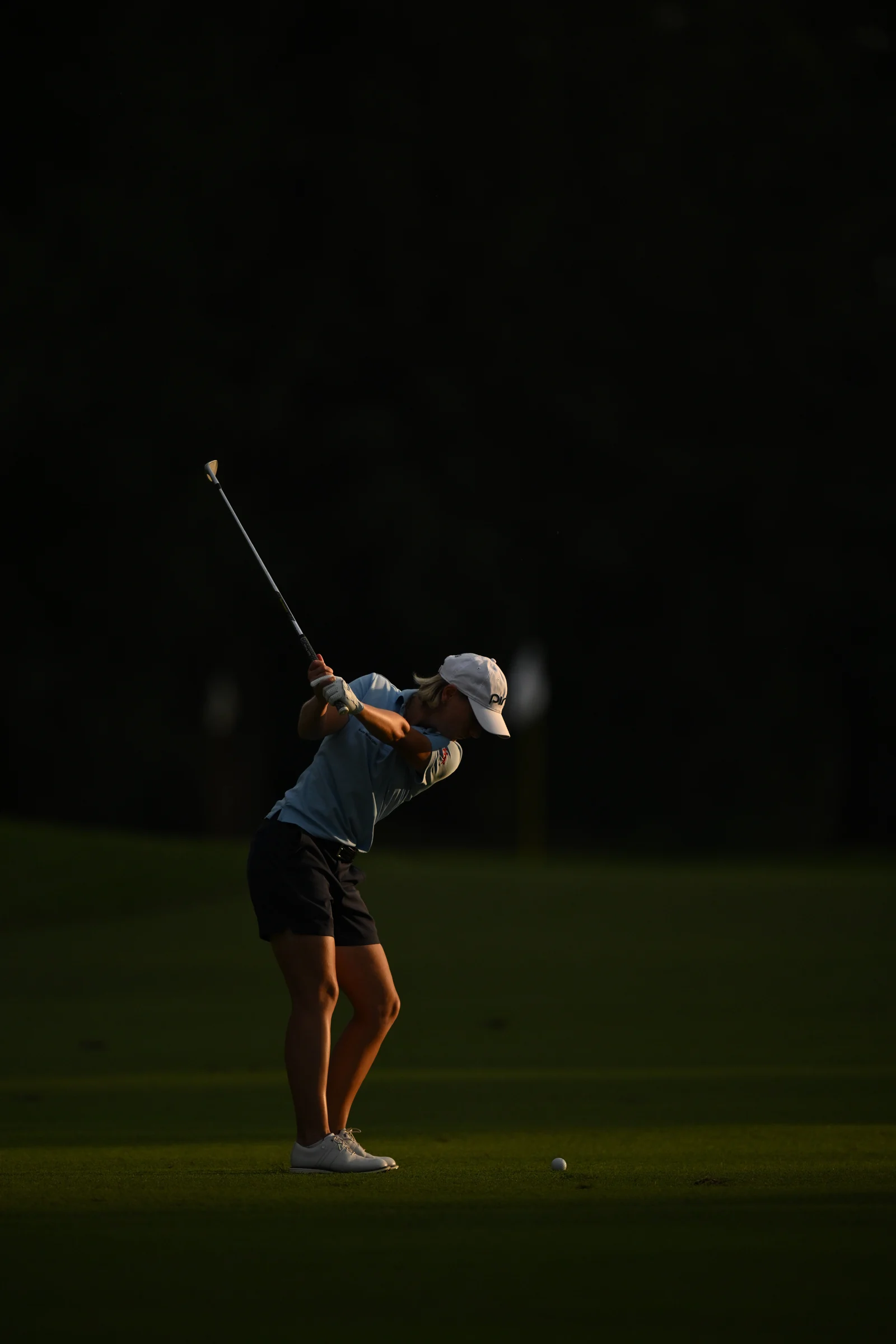 Dorota Zalewska podczas zamachu kijem golfowym na tle ciemnej zieleni